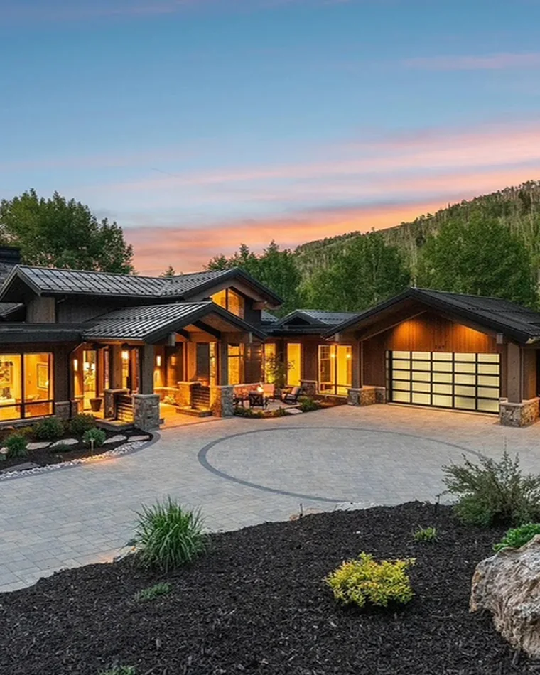 Mountain home at sunset with lit garages and a stone drive